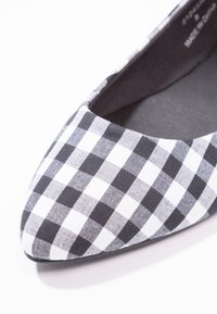 Plochá bota s špičatou špičkou s černobílým kostkovaným vzorem a černým vnitřním podšívkou na bílém pozadí.