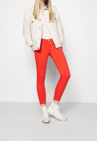 Rode skinny jeans met een hoge taille, gecombineerd met een crèmekleurige spijkerjack en witte high-top sneakers. Glad textuur, getailleerd ontwerp.