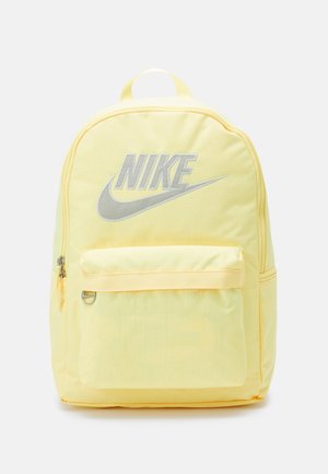 Sac à dos jaune Nike avec poche avant zippée et logo Nike argenté avec swoosh sur le compartiment principal sur fond uni.