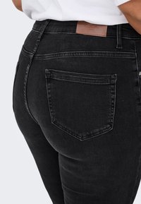 Melnas džinsa bikses ar piegulošu dizainu, aizmugurē ar ādas uzpirkstu un divām kabatām. Gluda tekstūra ar minimālām šuvēm.