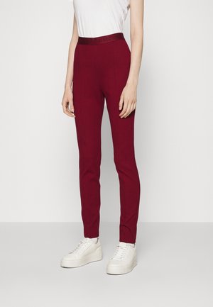 Pantalons ajustés bordeaux avec une texture lisse et une taille élastique. Associés à des baskets blanches, mettant en avant un look décontracté et moderne.