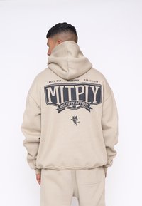 Felpa oversized beige con una grande stampa grafica nera sul retro con la scritta "MITPLY" e "MULTIPLY APPAREL", e cappuccio con cordino.
