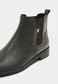 Musta nahkasaapas nilkkamittaisella, tekstuurilla varustetulla sivupaneelilla, elastisella insertillä ja matalalla lohkakannalla. Sivulla on hillitty logotieto.