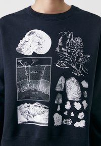 Felpa nera che presenta diverse grafiche bianche, tra cui un teschio, diagrammi geologici e formazioni rocciose, con una finitura in tessuto texturizzato.