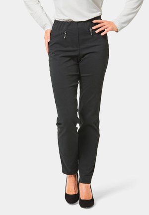 Schwarze Slim-Fit-Hosen mit Reißverschlusstaschen vorne, elastischem Bund, glatter Textur und schmal zulaufenden Beinen, kombiniert mit schwarzen High-Heels.