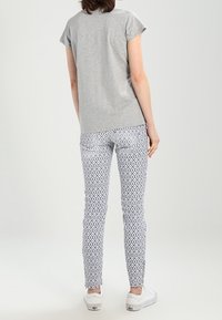 Camiseta de algodón gris de manga corta, combinada con pantalones blancos que presentan un patrón de diamantes azules, y zapatillas blancas.
