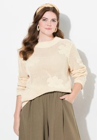 Maglione a maglia crema con motivi floreali, scollatura rotonda e maniche lunghe, abbinato a pantaloni a gamba larga plissettati di colore verde oliva.