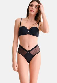 Ensemble de lingerie noire comprenant un soutien-gorge rembourré avec un bord en dentelle et une culotte taille haute. La culotte présente des panneaux en tulle à pois et des accents décoratifs.