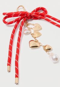 Red ribbon bow with white stripes, featuring gold heart charms and a pearl pendant. Includes hanging chains and metal accents.