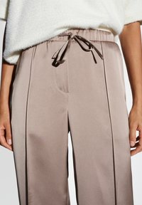 Beige wijde broek met een gladde textuur, featuring een trekkoord in de taille en zijzakken. Geaccentueerd met subtiele tonale strepen.