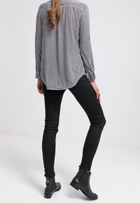 Camicia a maniche lunghe a quadri bianco e nero con bordo arrotondato, abbinata a jeans neri slim-fit e stivali neri alla caviglia, che mostrano un design elegante.