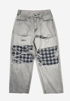 Ανοιχτό γκρι τζιν παντελόνι με μεγάλες φθαρμένες τρύπες στους μηρούς, που αποκαλύπτουν μαύρα και λευκά καρώ υφασμάτινα μπαλώματα από κάτω.