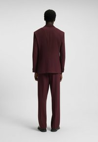 Burgundy suit with a structured blazer and wide-leg trousers. Material appears smooth; blazer features a single vent and buttoned cuffs.