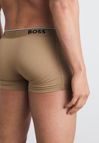 Beige színű boxer nadrág, testhezálló fazonnal, kontrasztos fekete logóval a derékpánton. Puha, rugalmas anyag, sima felület.