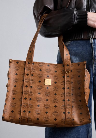 Brau tote soma, kas izgatavota no teksturēta sintētiskā materiāla. Iekļauj melnus logotipus un dimanta rakstus, ko papildina zelta piederumi un rāvējslēdzējs.
