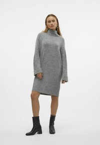 Abito grigio a maglia con collo alto, spalle cadenti e maniche lunghe. Texture morbida con polsini a coste. Indossato con stivali alla caviglia neri.
