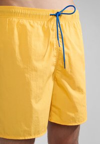 Geel zwemboxers met een elastische tailleband en een blauwe trekkoord, gemaakt van een gladde, lichtgewicht stof. Korte lengte met minimale ontwerpdetails.