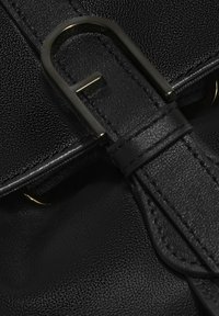 Dettaglio di una borsa in pelle nera con superficie testurizzata, accenti cuciti e una fibbia metallica con un design a "F".