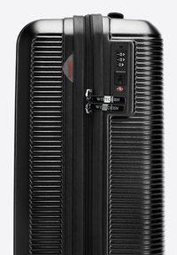 Valise rigide noire avec texture rainurée, double zips, serrure à combinaison et accents de logo, fabriquée en matériau polycarbonate durable.