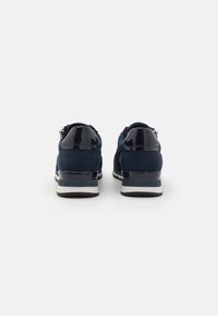 Sneakers blu navy con un mix di suede opaco e dettagli in vernice lucida, caratterizzati da un tallone imbottito e una suola testurizzata per una maggiore aderenza.