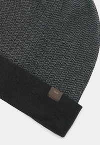 Dunkelgraue und schwarze Strickmütze mit Chevron-Muster und einem kleinen braunen Etikett mit dem Markennamen Liu Jo am Rand.