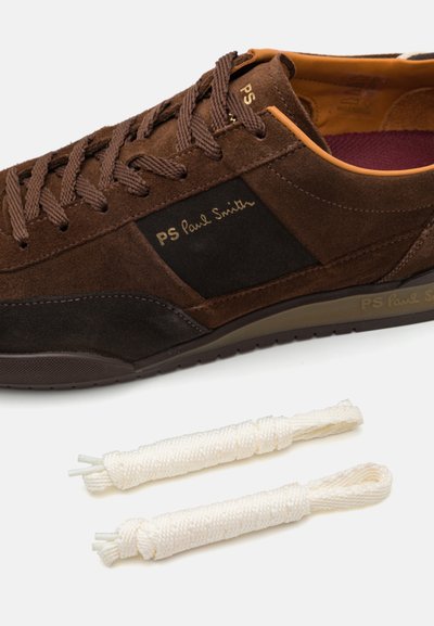 Brown suede sneaker with black accents, flat laces, and branding. Includes two extra cream-colored laces. Features a textured rubber sole.