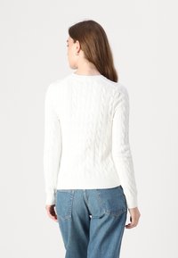 Pull en maille blanche à col rond avec des manches longues et un ourlet côtelé, associé à un jean en denim bleu. Le design présente un motif texturé.