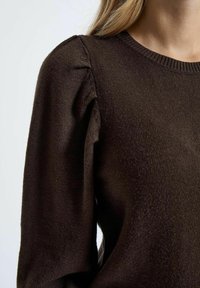 Brown knitted sweater with a round neckline and puffed sleeves. Soft texture with a smooth finish, showing slight ribbed detailing at the neck.