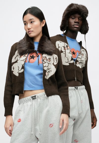 Brun stickad cardigan med pälskrage med tecknade figurer, kombinerad med en blå T-shirt och grå mjukisbyxor med kyssavtryck.