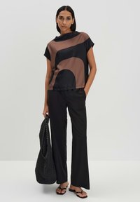 Top di seta con motivi astratti marroni e neri, abbinato a pantaloni larghi neri e a una borsa nera texturizzata. Il modello indossa sandali flat.