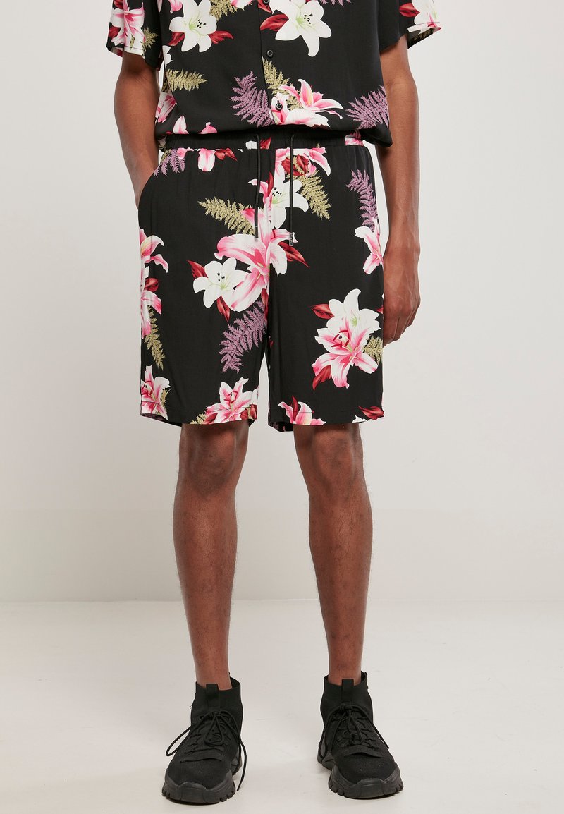Ensemble comprenant une chemise à fleurs noires et un short, mettant en avant de grandes lys roses et des accents verts. Le tissu est léger avec une taille élastique.