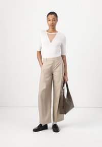 Hvit kortermet topp med v-hals, parret med beige vide bukser og svarte loafers. En brun skulderveske fullfører antrekket.