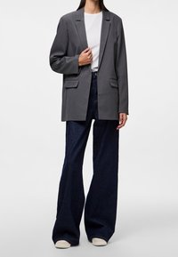 Blazer gris avec revers crantés et deux poches avant, associé à un jean foncé taille haute évasé et des baskets blanches. Texture de tissu lisse.