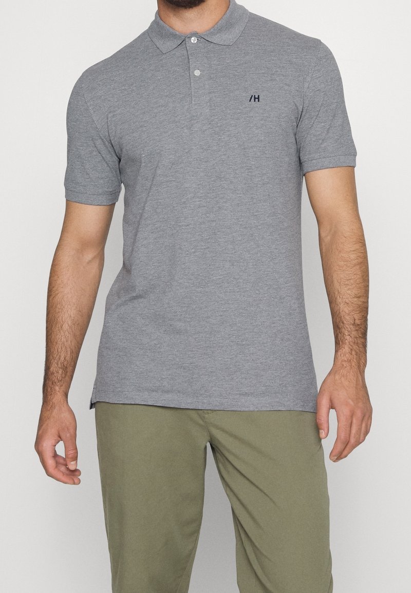 Szary polo z bawełny z kołnierzykiem i dwoma guzikami. Posiada małe ciemne logo na piersi oraz krótkie rękawy.