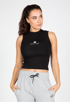Zwarte mouwloze crop top van goed aansluitend jersey stof, met een wit logo in het midden, gecombineerd met lichtgrijze broek met trekkoord.