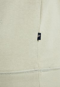 Tissu en polaire vert clair avec une texture côtelée. Présente des coutures contrastantes et une petite étiquette marine sur le côté.