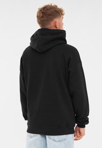 Sudadera negra con una gran capucha, mangas largas y puños de canalé. Hecha de material suave, presenta un corte relajado y sin marcas visibles.