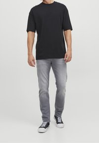 Camiseta negra de algodón con mangas cortas, combinada con jeans de mezclilla gris claro y zapatillas negras con suelas blancas y cordones blancos.