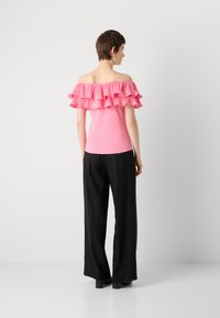 Top rosa de tirantes caídos con volantes en capas, ajustado al cuerpo, combinado con pantalones anchos negros y zapatos de tacón cuadrado. Textura simple y suave.