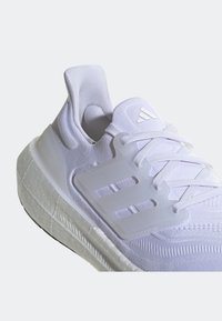 Baskets de sport blanches avec tige en maille texturée, cage à lacets en plastique, semelle intermédiaire amortie et logo Adidas sur la languette, vue inclinée de gauche.