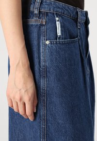 Denim skirt in dark blue with visible stitching, five-pocket design, and a small label. Smooth texture and straight cut.
