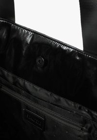 Interiorul unei genți negre, cu un material strălucitor și neted, prevăzut cu închidere magnetică și un buzunar cu fermoar, completat de un model texturat.
