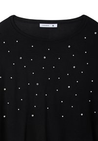 Maglione nero a maglia con borchie bianche e metalliche sparse. Collo rotondo e maniche corte, texture liscia, design semplice. Taglia S.