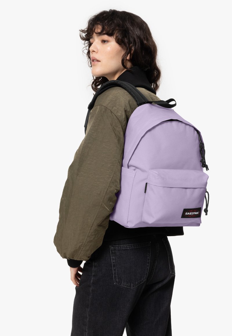 Liila reppu, jossa on vetoketjullinen sulku, etutasku ja säädettävät hihnat; valmistettu kestävästä kankaasta; logo-tarra edessä.