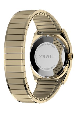 Ρολόι χειρός Timex σε χρυσό τόνο με μεταλλικό λουρί από κρίκους, δείχνοντας την πίσω πλευρά από ανοξείδωτο ατσάλι με χαραγμένο το σήμα, την αντοχή στο νερό και τις λεπτομέρειες του αυτόματου μηχανισμού.