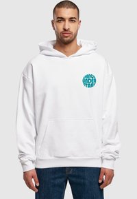 Sudadera blanca con un gran bolsillo frontal, con un gráfico circular en color teal que dice "Baila Bajo las Estrellas". Tejido de textura suave.