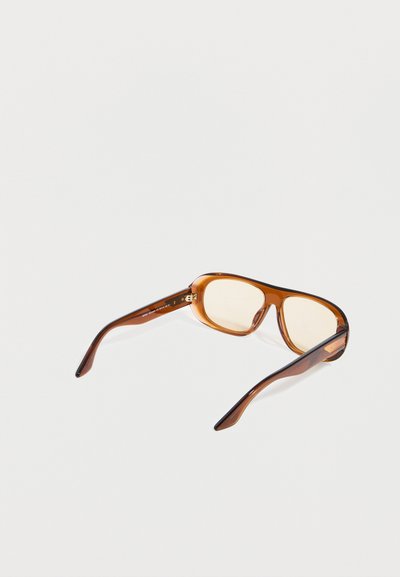 Καφέ διαφανή ορθογώνια γυαλιά με φακούς ελαφρώς χρωματιστούς, τοποθετημένα σε λευκή επιφάνεια, στραμμένα ώστε να φαίνεται η εσωτερική πλευρά του σκελετού.