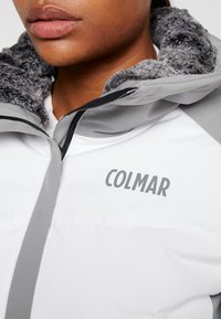 Vit pufferjacka med grå detaljer och krage i päls. Har dragkedja och "COLMAR"-logotyp på bröstet.