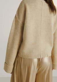 Beżowy sweter dzianinowy o prążkowanej fakturze i opadających ramionach, połączony z błyszcząco złotą spódnicą plisowaną. Przytulny, luźny krój.