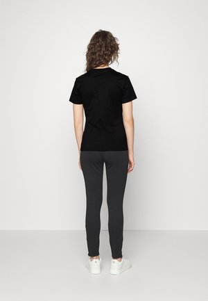 Black cotton t-shirt with short sleeves, paired with dark gray fitted pants and white sneakers, viewed from the back on a plain background.